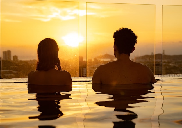 Siluetta delle coppie amorose nell'acqua del palo dell'infinito durante il tramonto. concetto di vacanza romantica.
