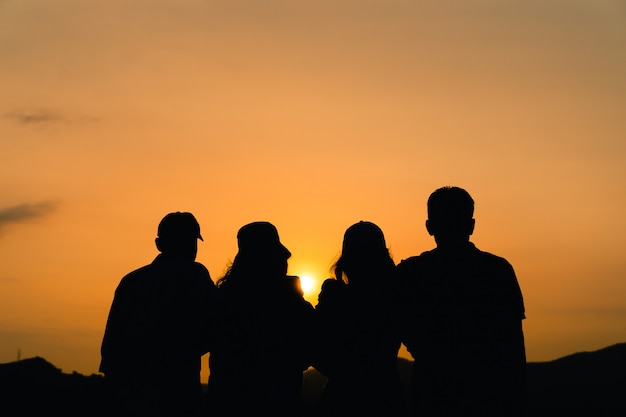 Foto siluetta degli amici maschii e femminili che si abbracciano che esamina l'alba. felicità, successo, amicizia e concetti di comunità.