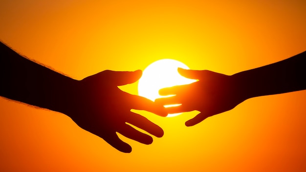 Silhouette of male and female hands on the background of the setting sun. concept of communication and striving for closeness in society and family