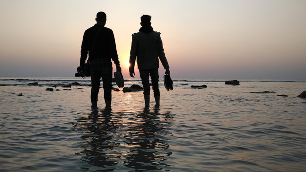 Silhouette male friends standing in sea during sunset