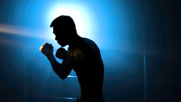 Silhouette of man athlete standing and doing shadow boxing exercises in gym