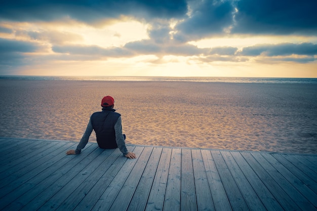 Силуэт мужчины на пляже, смотрящего на волшебный закат Мужчина сидит на деревянной террасе