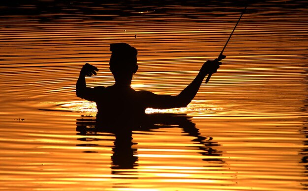 Foto silhouette di un uomo sul lago contro il cielo durante il tramonto