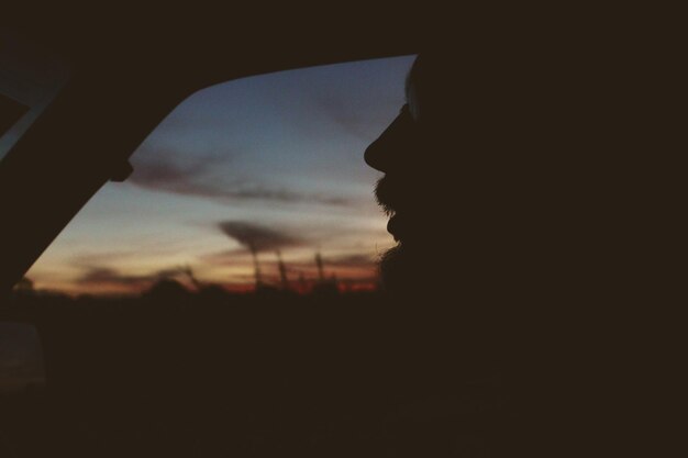 Silhouette man in car against sky during sunset