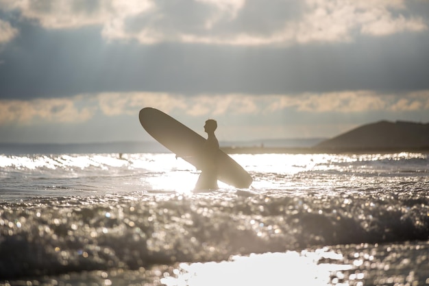 Foto uomo a silhouette che porta una tavola da surf in mare