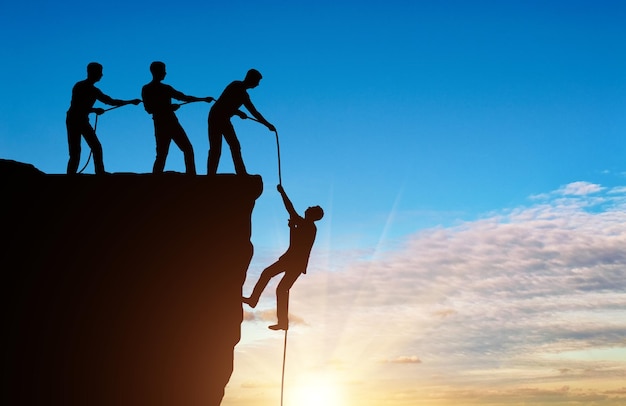 Photo silhouette of a man climbers pulling out of a cliff of another climber. conceptual scene of male mountaineers work in the same team