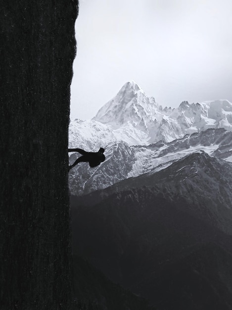 Foto uomo a silhouette che si arrampica su una montagna rocciosa contro un cielo limpido
