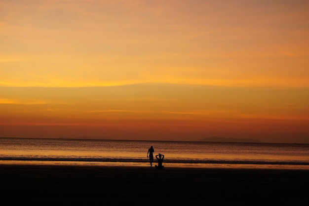 Silhouette man doing yoga by friend at beach against sky during sunset