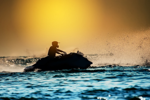 Foto silhouette di uomo guida freestyle jet ski al tramonto. il cavaliere professionale fa acrobazie in mare