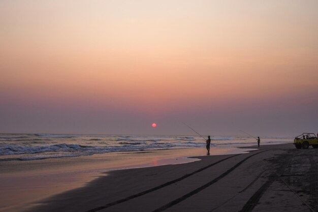 Silhouette of a man fishing at the beach during the sunset