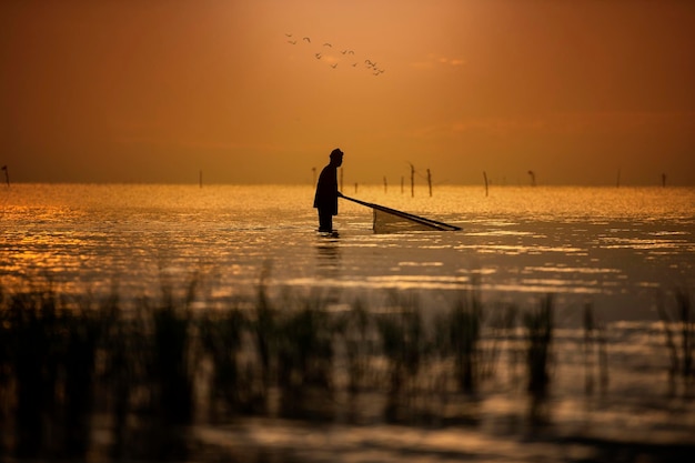 写真 夕暮れの空に逆らって海で釣りをしている男性のシルエット