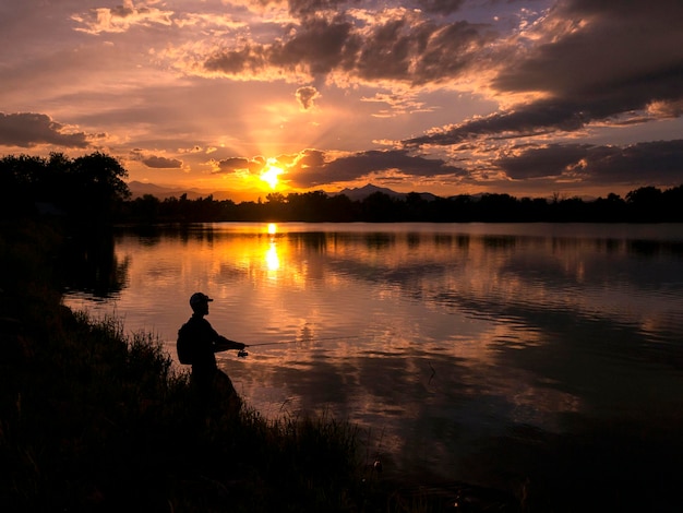 夕暮れの空を背景に湖で釣りをしている男性のシルエット
