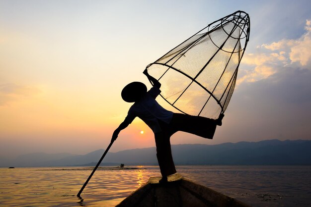 夕暮れの空を背景に湖で釣りをしている男性のシルエット