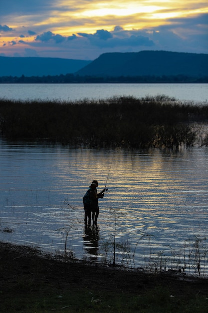 夕暮れの空を背景に湖で釣りをしている男性のシルエット