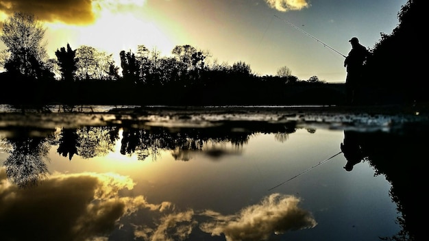 Photo silhouette man fishing in lake during sunset