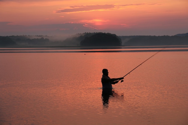 Силуэт человека, ловящего рыбу в озере во время захода солнца