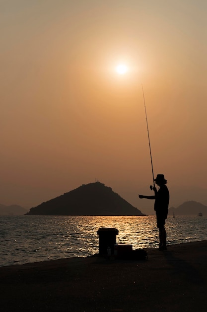 Foto silhouette di un uomo che pesca in mare contro il cielo durante il tramonto