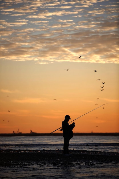 Foto silhouette di un uomo che pesca in mare contro il cielo durante il tramonto