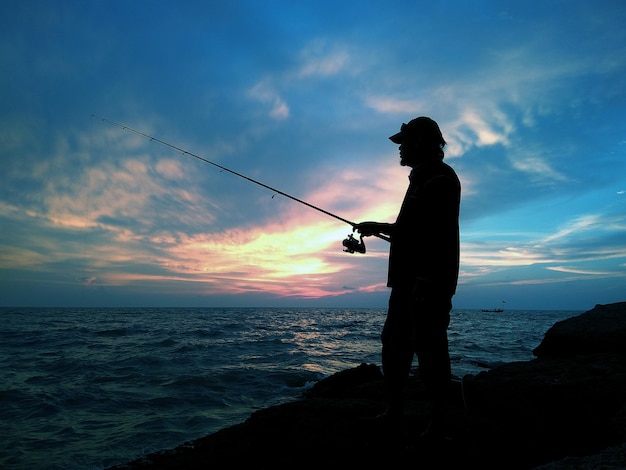 Photo silhouette man fishing on sea against sky during sunset