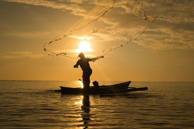Силуэт человека, ловящего рыбу в море на лодке на фоне неба во время захода солнца