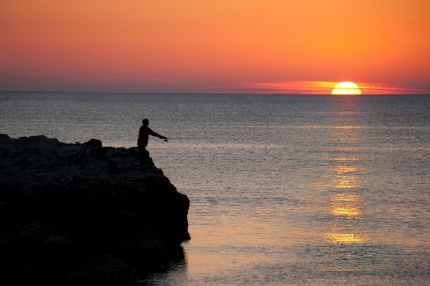 夕暮れ時の海で釣りをする男のシルエット