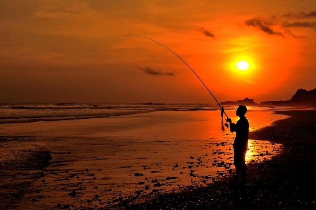 Silhouette man fishing on shore against sky during sunset