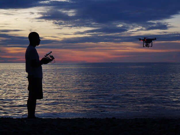 写真 夕暮れの空に向かって海を飛ぶ無人機のシルエットマン