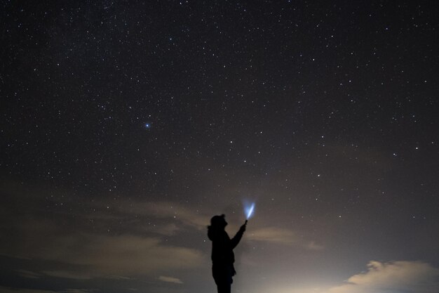 写真 夜に星のフィールドに立ち向かって照らされた ⁇ 中電灯を握っているシルエットの男性