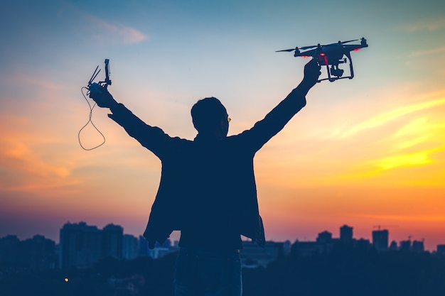 Silhouette of man holding switched on drone quad copter and remote control enjoying freedom victory