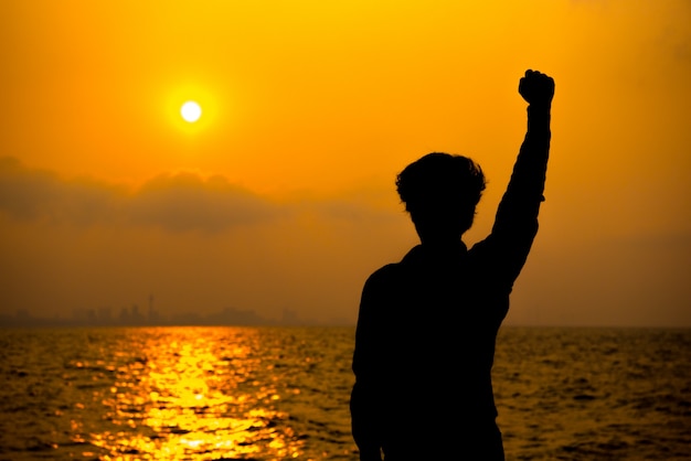 silhouette of behind a man is standing to looking sunset on city beside sea