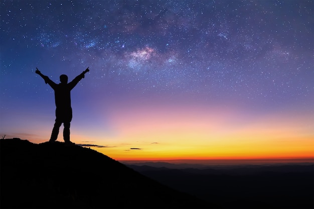 Silhouette of man is standing on top of mountain and spreading hand