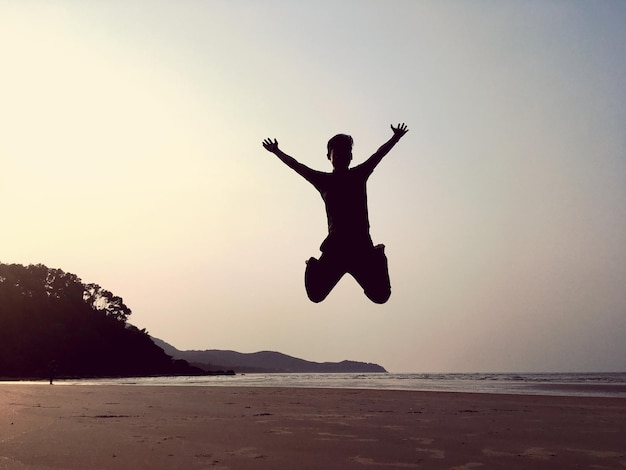 Foto uomo a silhouette che salta sulla spiaggia contro il cielo