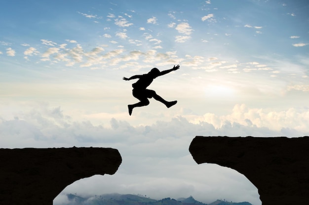 Silhouette man jumping over cliffs against cloudy sky