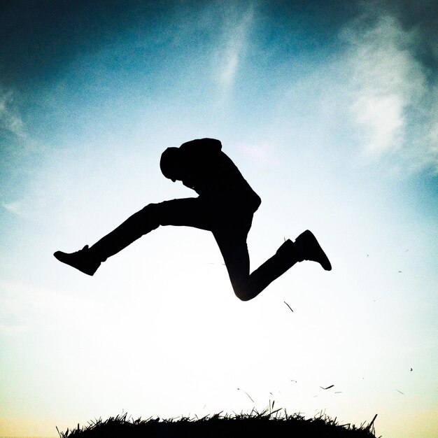 Photo silhouette man jumping above grass against sky