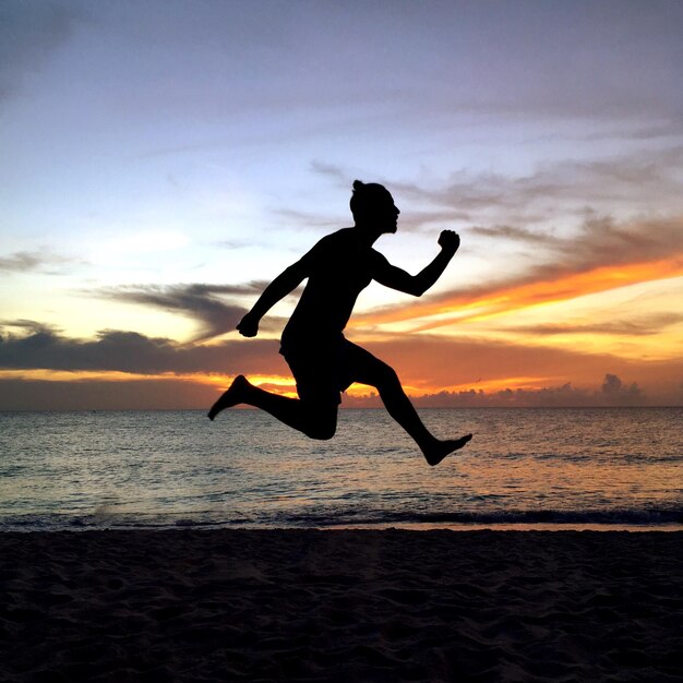 사진 해가 지는 동안 해변에서 하늘을 향해 점프하는 실루 남자