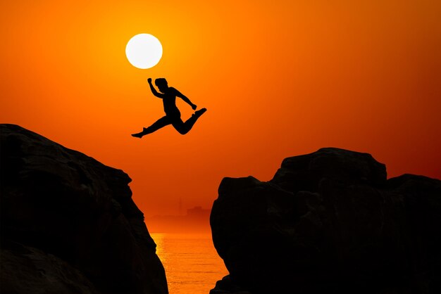 Foto silhouette di un uomo che salta su una roccia sulla spiaggia durante il tramonto