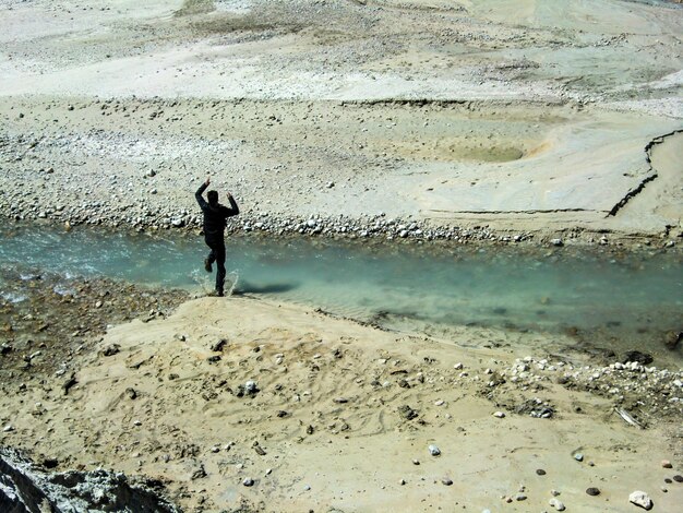 silhouette of man jumping between a small stream