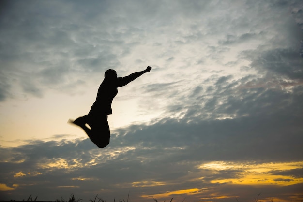 Photo silhouette of a man jumping with happy in the sunset.