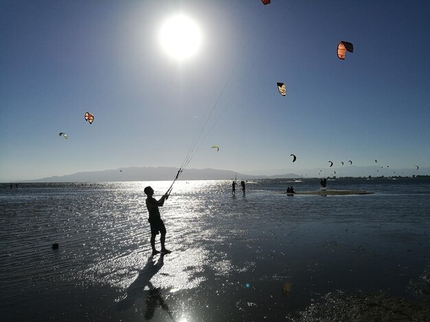 Photo silhouette man kiteboarding at beach during sunset