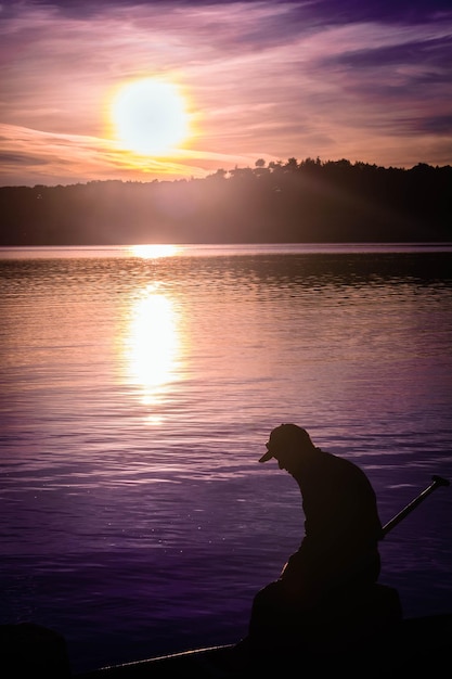 Photo silhouette man at lake against sky during sunset