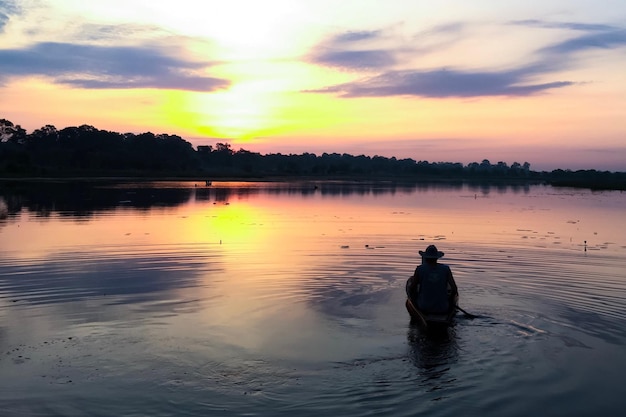 Silhouette man in lake against sky during sunset