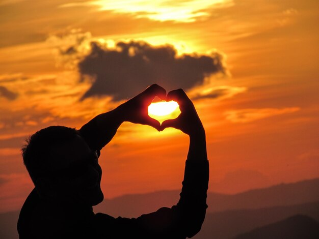 Photo silhouette man making heart shape with hands against sky during sunset