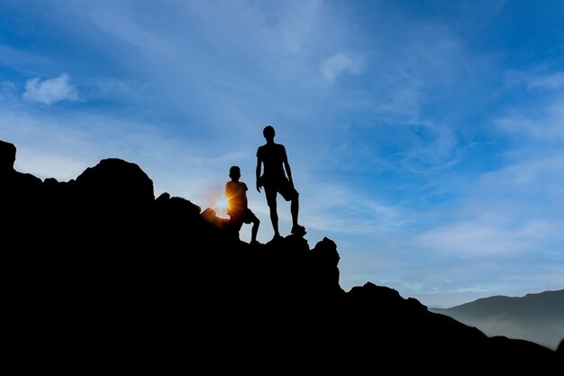 Silhouette of a man and a man on a mountain and blue sky