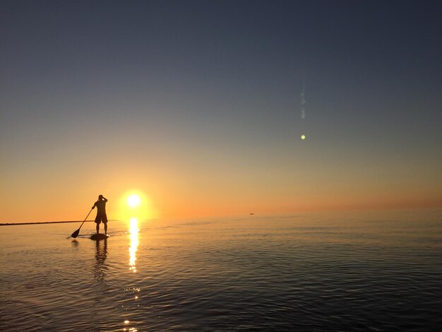 Silhouette man paddleboarding in sea against clear sky