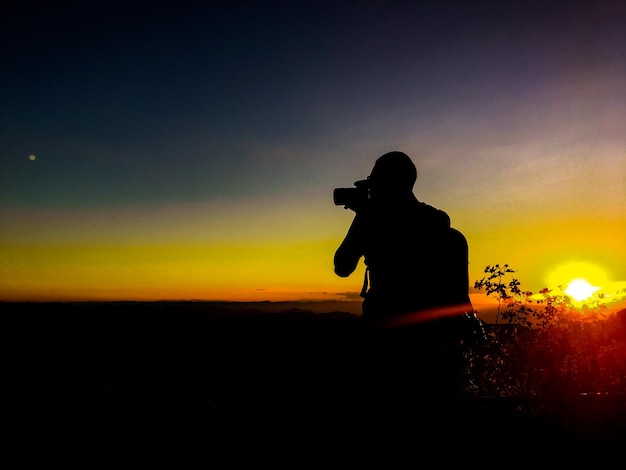 Silhouette man photographing against orange sky during sunset