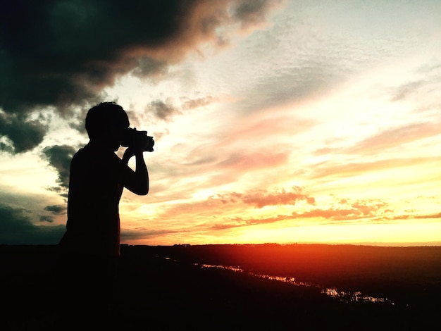 Silhouette man photographing against sky during sunset