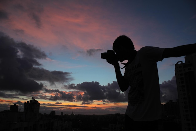 夕暮れの空を背景に都市風景を撮影するシルエットの男性