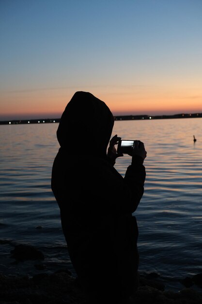 Photo silhouette man photographing sea against sky during sunset