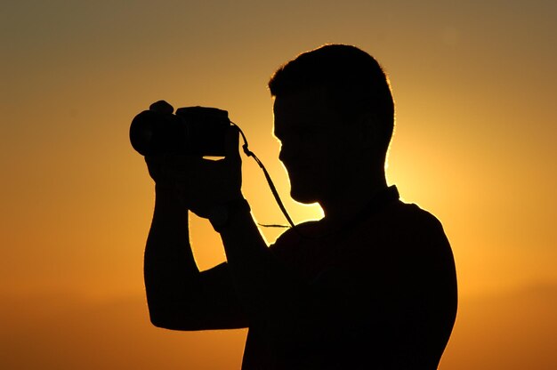 写真 空に向かってカメラで写真を撮っているシルエットの男性