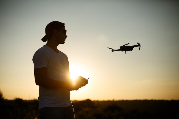 Silhouette of a man piloting drone in the air with a remote controller in his hands on sunset pilot